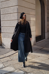 a lady in a black knit top, a pair of wide leg jeans and a black long wool coat